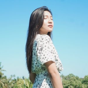 Young woman meditating on her breath while looking up at the sun in the blue sky