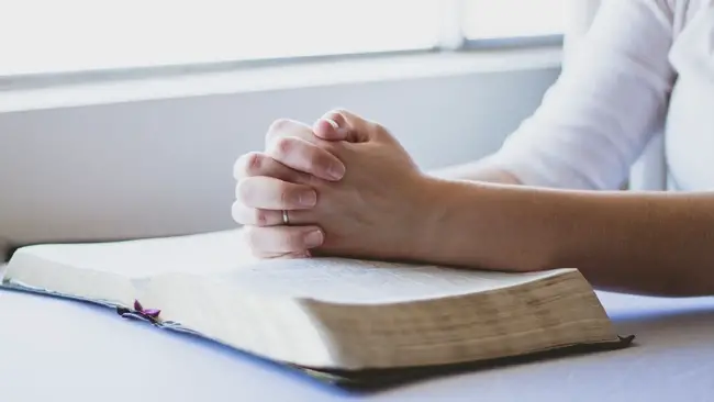 Christian meditation: Woman praying with her hands on an open Bible